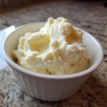 A white bowl filled with creamy, fluffy mashed potatoes sitting on a granite countertop.