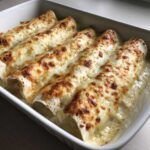 Close-up of baked white chicken enchiladas covered in bubbly, browned cheese sauce in a white baking dish.
