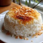 A perfectly molded serving of Bobby Flay's Crispy Coconut Rice with a golden-brown, toasted coconut crust on top.