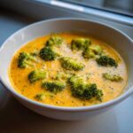 Close-up of creamy, vibrant orange Broccoli and Cheddar Soup topped with bright green broccoli florets.
