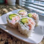 Four freshly cut pieces of California Sushi Roll featuring crab, avocado, and rice on a white plate.
