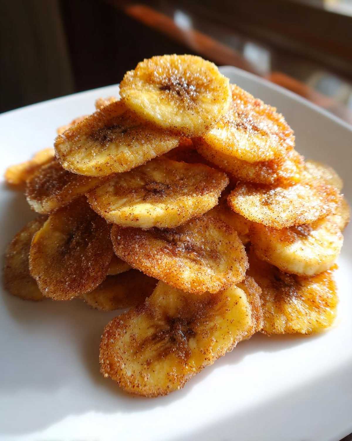 A close-up stack of golden, crispy Cinnamon Sugar Air Fryer Banana Chips dusted heavily with cinnamon and sugar.