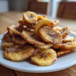 A mound of crispy Cinnamon Sugar Air Fryer Banana Chips piled high on a white plate.