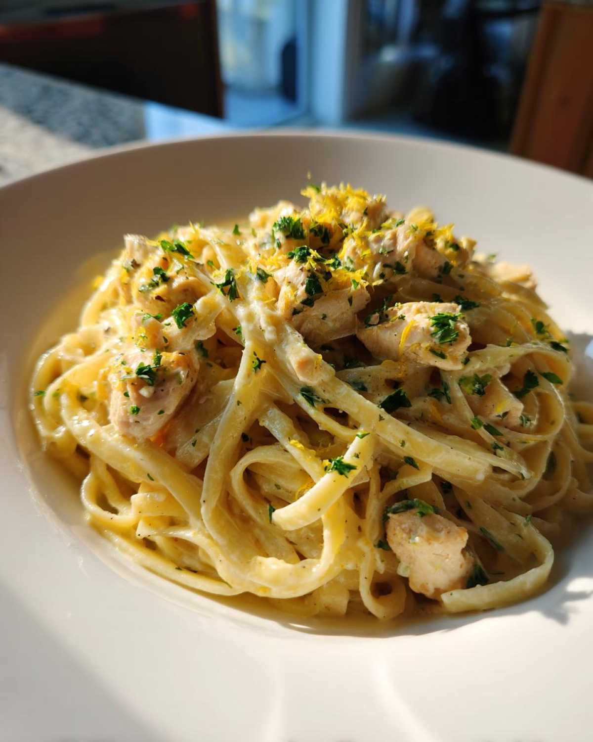 Close-up of a bowl of creamy Lemon Chicken Pasta garnished with bright yellow lemon zest and fresh green parsley.