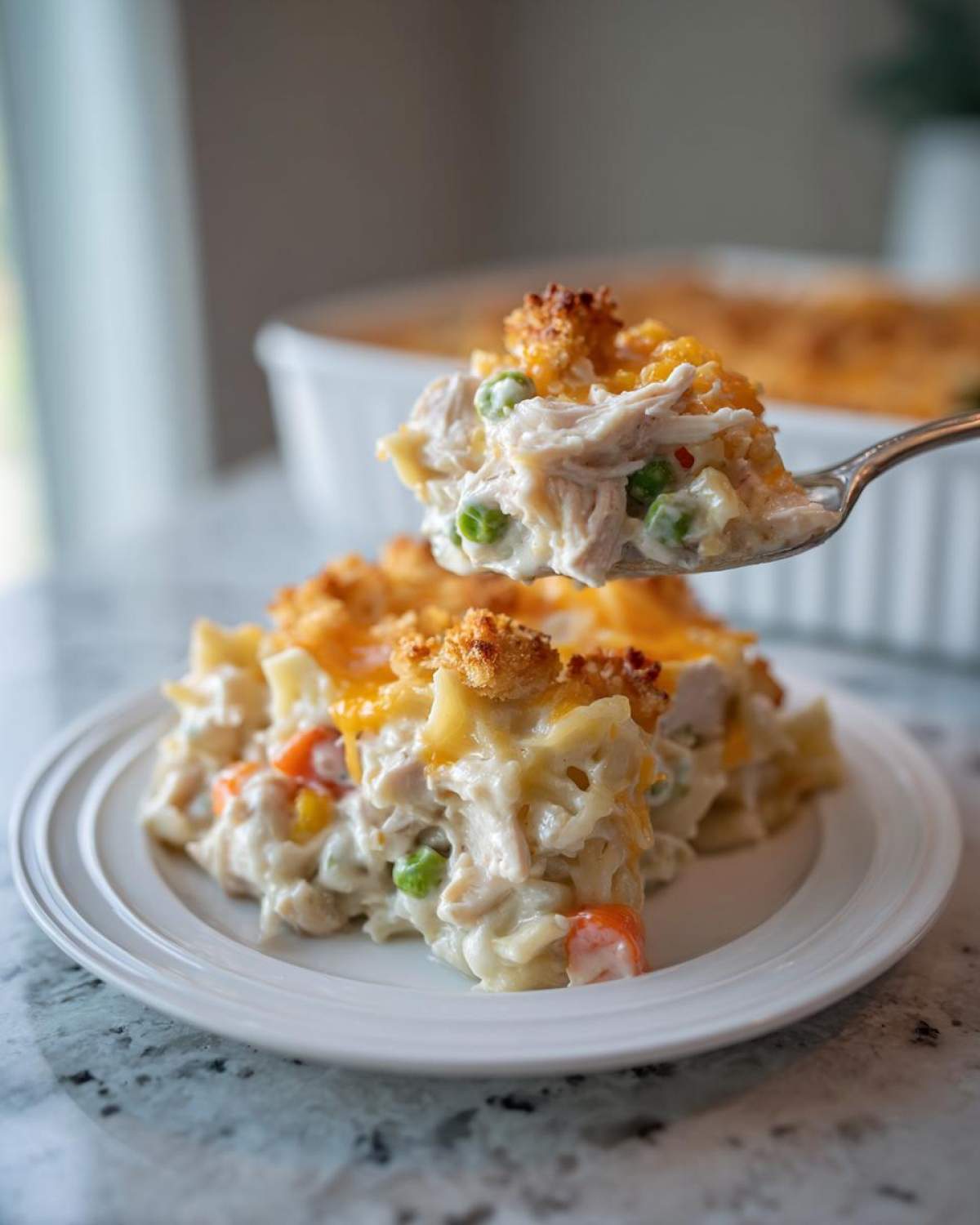 A spoonful of creamy Turkey Casserole lifted above a serving on a white plate, showing shredded turkey, peas, and cheesy topping.