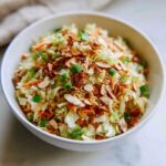 A close-up of a bowl filled with Crunchy Asian Ramen Noodle Salad, topped with almonds and green onions.