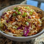 A white bowl filled with Crunchy Asian Ramen Noodle Salad, topped with peanuts and green onions.