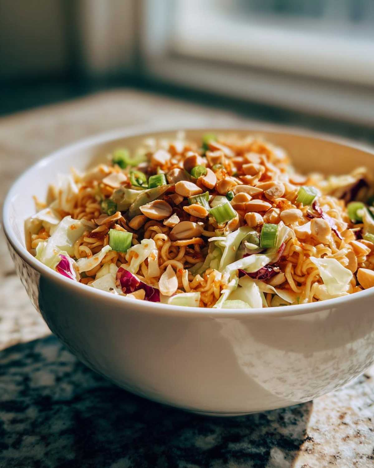 A close-up of Crunchy Asian Ramen Noodle Salad topped with peanuts and green onions in a white bowl.