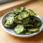 A close-up of a mound of crispy, seasoned Crunchy Ranch Cucumber Chips served on a light gray plate.