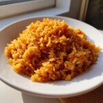 A close-up of a white bowl filled with fluffy, perfectly cooked Mexican Rice, brightly lit by sunlight.