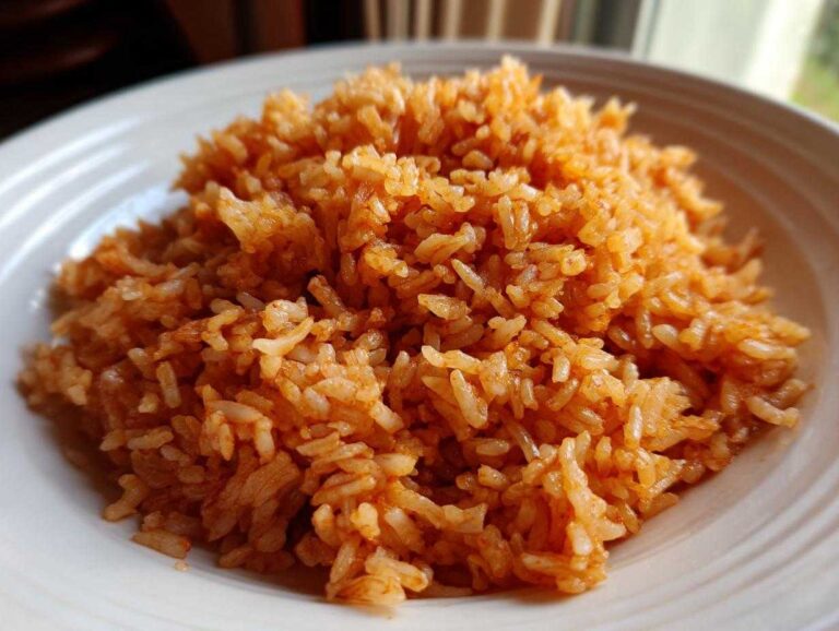 Close-up of a generous serving of fluffy, orange-red Mexican Rice piled high on a white, ridged plate.