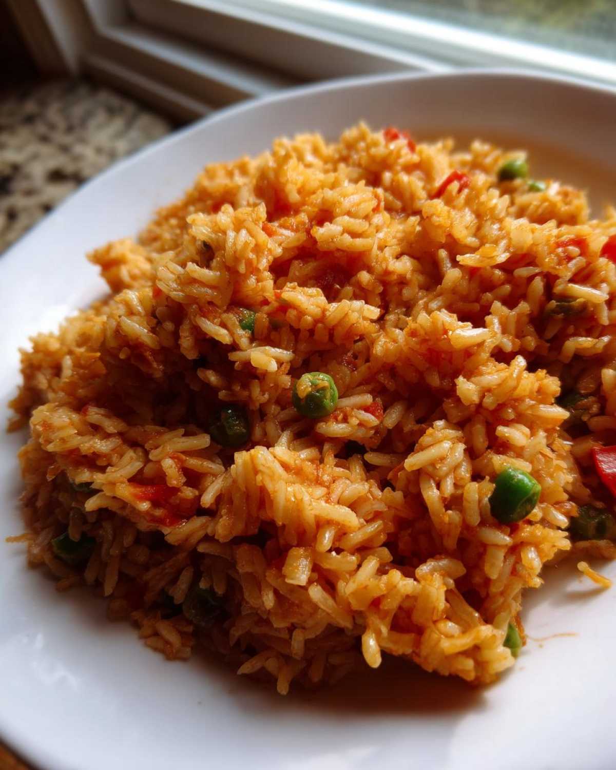 Close-up of fluffy, orange-tinted Spanish Rice mixed with green peas served on a white plate.