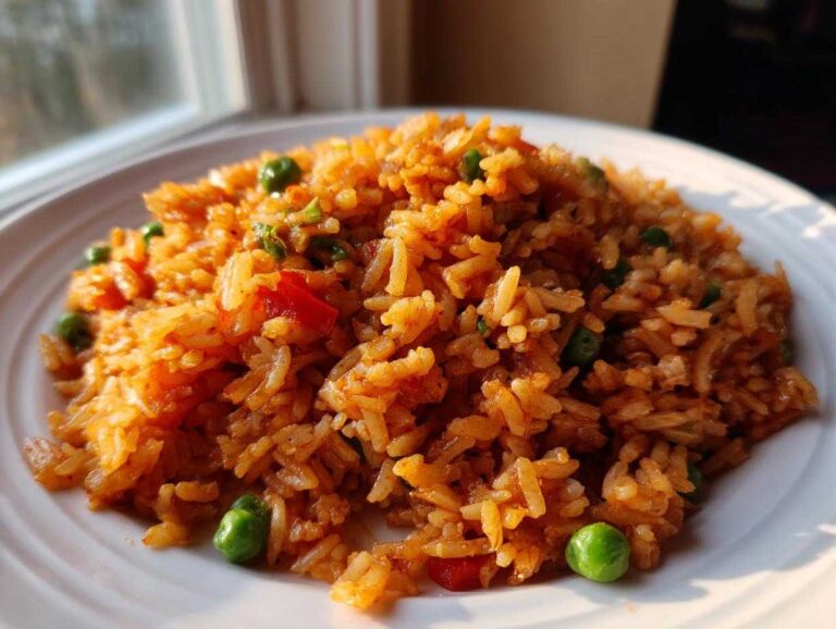 A close-up of fluffy, orange-hued Spanish Rice mixed with bright green peas and red peppers on a white plate.
