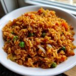Close-up of fluffy, orange-colored Spanish rice mixed with bright green peas and onions in a white bowl.