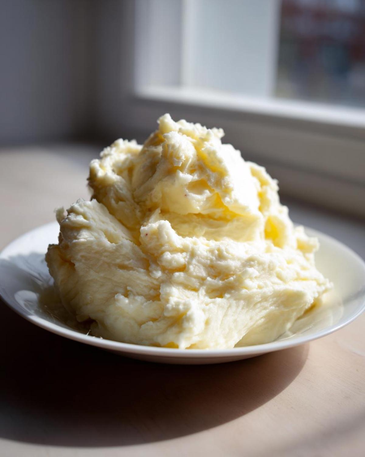 A generous mound of creamy, fluffy Steakhouse Potatoes served on a white plate, highlighted by natural window light.