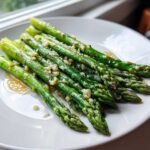 A serving of bright green Garlic Butter Asparagus 15 Minutes Lina, drizzled with melted butter and topped with minced garlic, on a white plate.