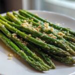 Bright green spears of Garlic Butter Asparagus 15 Minutes Lina, glistening with butter and topped with minced garlic, served on a white plate.