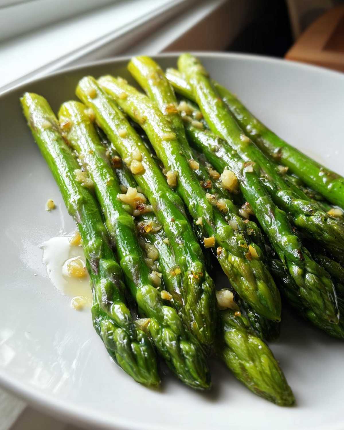 Close-up of bright green Garlic Butter Asparagus 15 Minutes Lina spears glistening with melted butter and minced garlic on a white plate.