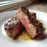 Two thick slices of medium-rare Garlic Rosemary Lamb Chops resting in lemon butter sauce on a white plate.
