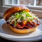 Close-up of a juicy Gochujang Chicken Burger with melted cheese, slaw, and green onions on a toasted bun.