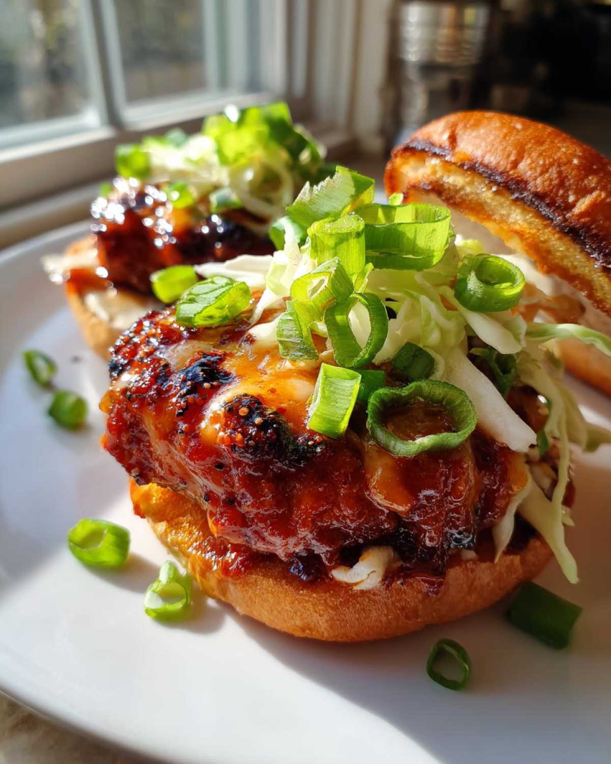 Close-up of a delicious Gochujang Chicken Burger patty covered in spicy glaze, topped with slaw and green onions.