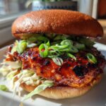Close-up of a juicy Gochujang Chicken Burger featuring a glossy, caramelized patty topped with fresh green onions.