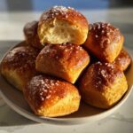 A stack of warm, golden brown Pretzel Bites topped with coarse salt, one broken open to show the soft interior.