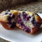 Close-up of a Greek Yogurt Blueberry Muffin cut in half showing a moist, berry-filled interior on a white plate.