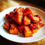 Close-up of glistening, caramelized Honey Cinnamon Roasted Sweet Potatoes piled on a white plate.