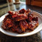 Close-up of sticky, glazed Korean BBQ Chicken pieces sprinkled with sesame seeds on a white plate.