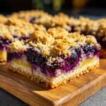 A close-up, appetizing shot of a thick slice of Lemon Blueberry Streusel Bars showing the bright purple blueberry layer and golden crumble topping.