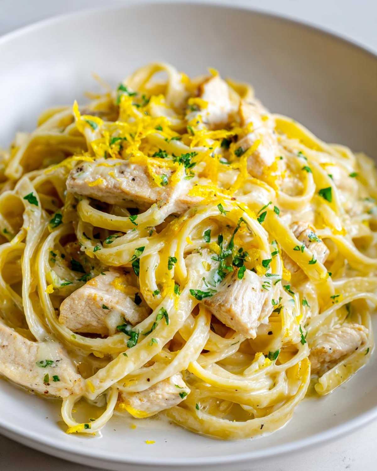 Close-up of creamy Lemon Chicken Pasta featuring fettuccine, diced chicken, and bright yellow lemon zest.