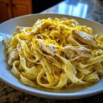 A close-up bowl of creamy Lemon Chicken Pasta topped generously with bright yellow lemon zest and herbs.