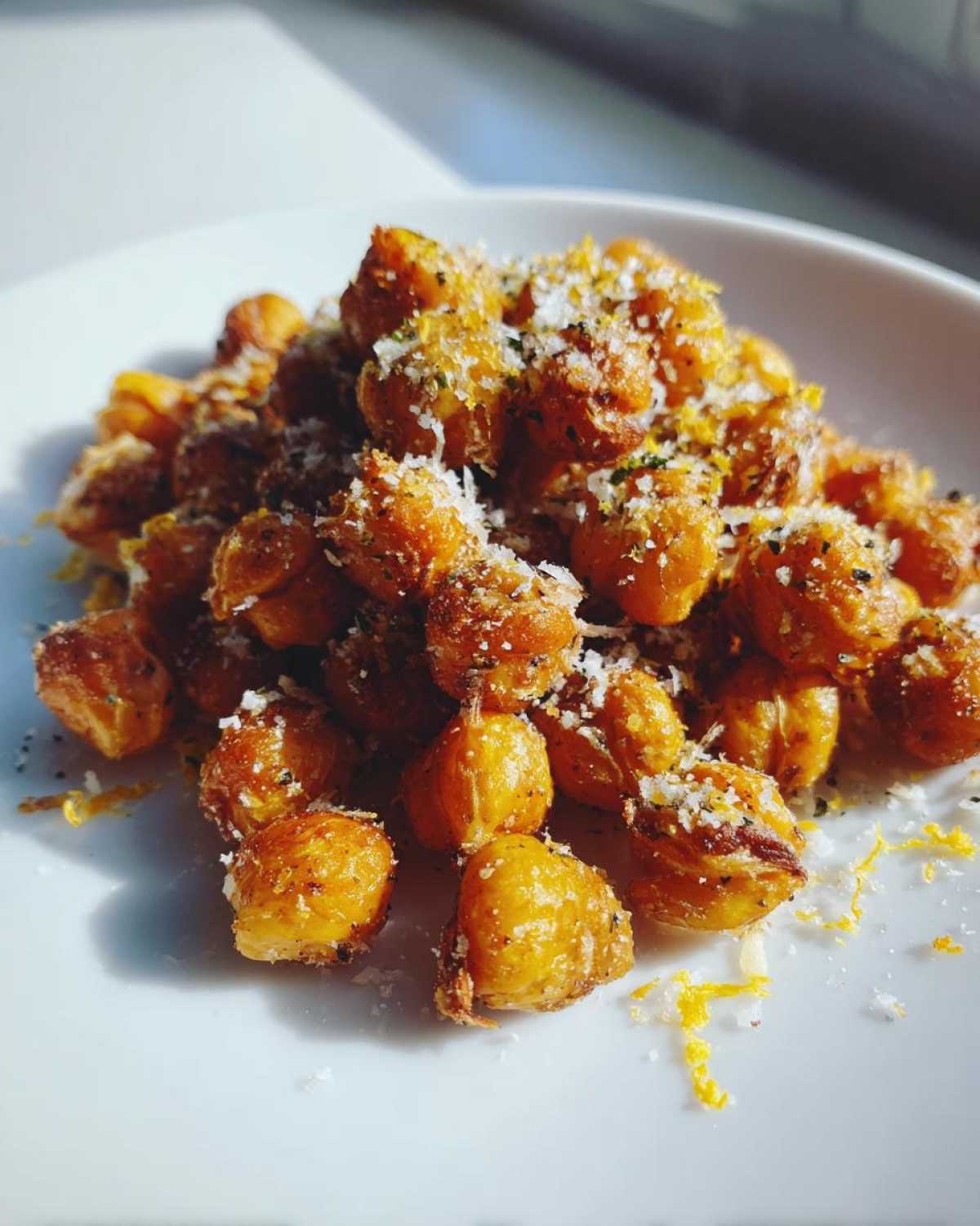 Close-up of crispy, golden Lemon Parmesan Roasted Chickpeas sprinkled with grated cheese and zest on a white plate.