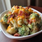 A close-up of a creamy Loaded Broccoli Cauliflower Salad Low Carb topped with shredded cheddar cheese and crispy bacon pieces.
