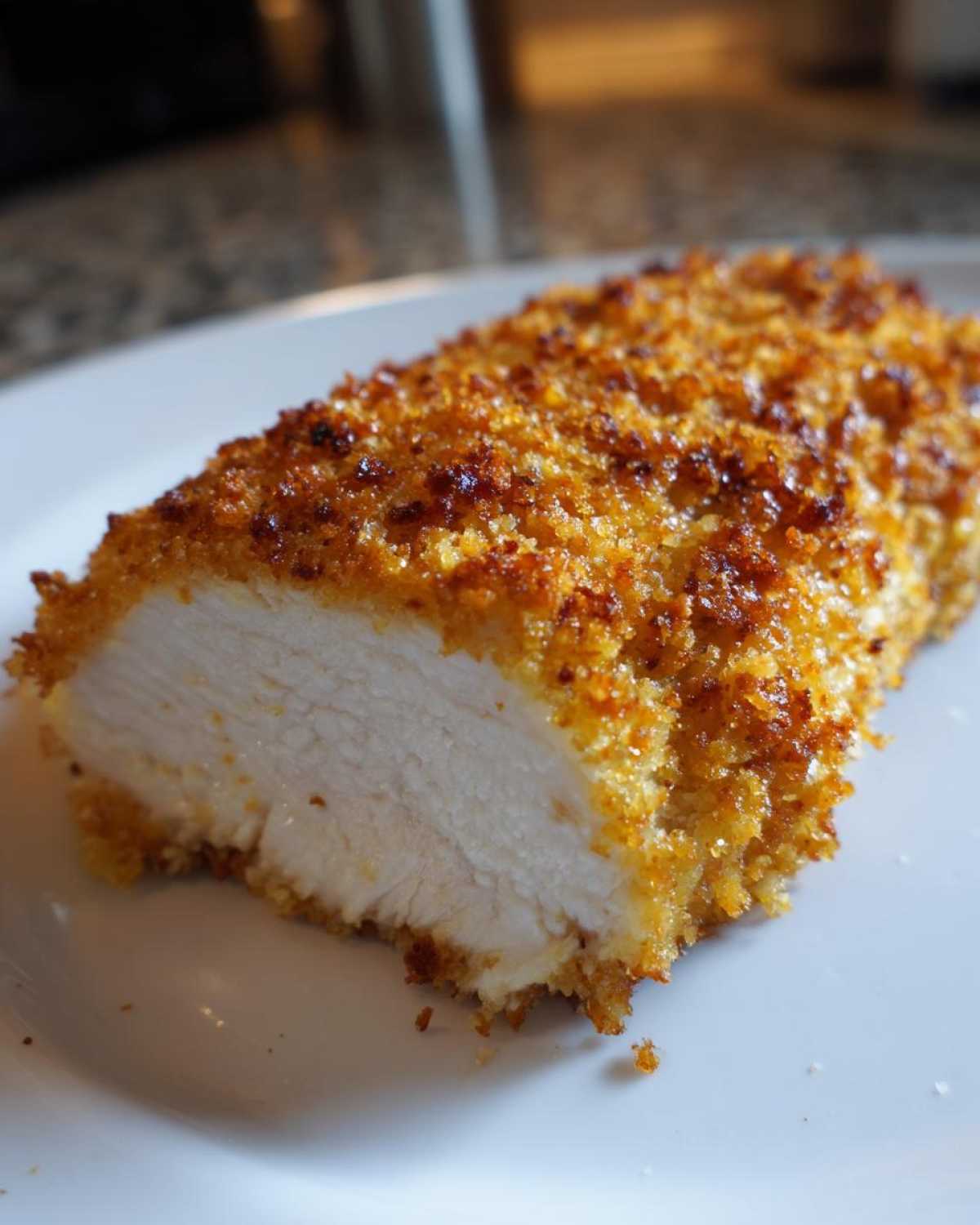 Close-up of a cooked Longhorn Steakhouse Parmesan Chicken breast, showing the juicy white interior and golden, crispy breaded crust.