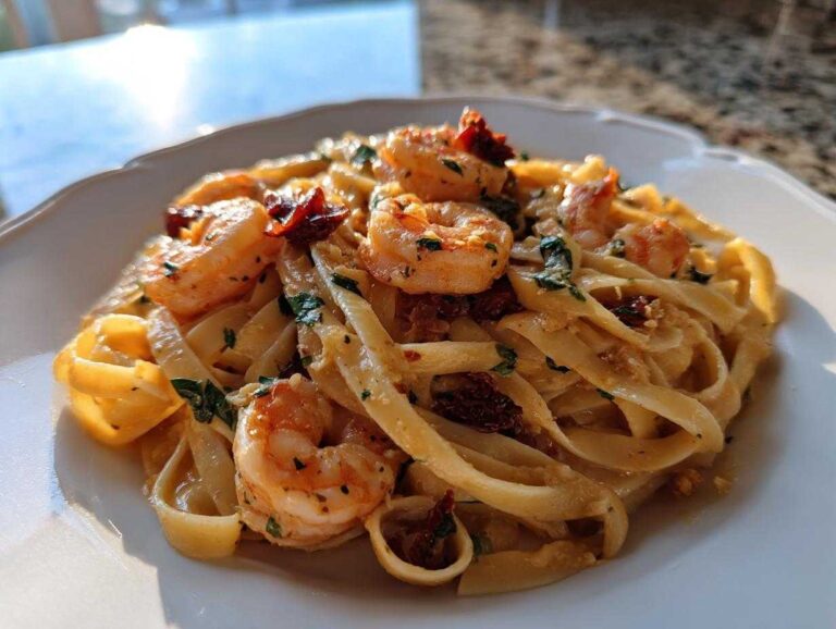 Close-up of creamy Marry Me Shrimp Pasta featuring large shrimp and sun-dried tomatoes on a white plate.