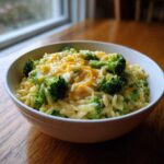 A close-up of a white bowl filled with creamy One Pot Broccoli Cheese Orzo topped with melted cheddar.