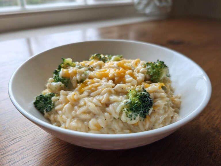 A close-up of creamy One Pot Broccoli Cheese Orzo topped with melted cheddar cheese and bright green broccoli florets.