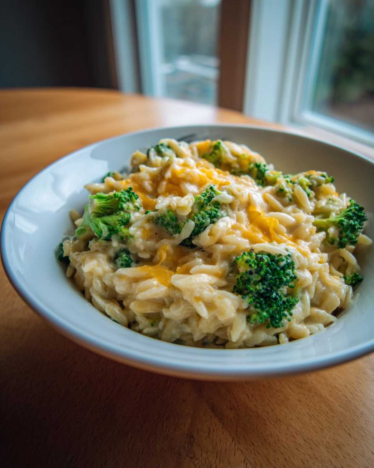 A close-up of a creamy bowl of One Pot Broccoli Cheese Orzo topped with melted cheddar.