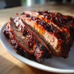 Close-up of thick, juicy slices of Slow Cooker Brisket covered in a rich, dark red glaze on a white plate.