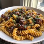 Close-up of fusilli pasta tossed in a rich sauce with sausage pieces, garnished with parsley and cheese for Sticky Honey Garlic Sausage Pasta Skillet.