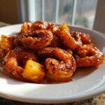 Close-up of glazed Sweet Chili Pineapple Shrimp pieces served on a white plate, glistening under natural light.